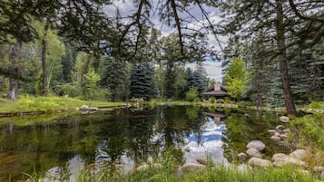 Un étang paisible, entouré d’une forêt dense, agrémenté d’un belvédère et d’une construction en pierre.