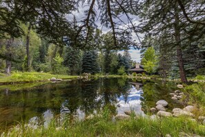 A tranquil pond surrounded by dense forest, a gazebo, and a stone structure.