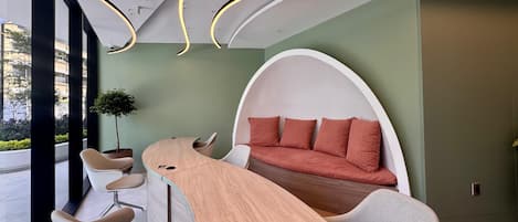 A modern interior with a curved wooden table, a unique seating area with a curved wall, and a view of the outdoors.