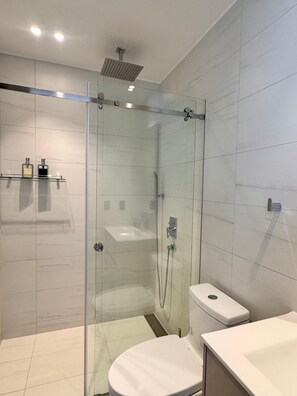A modern bathroom with a glass-enclosed shower, a white toilet, and a sink with a mirror. - Vrbo Property (Quito)