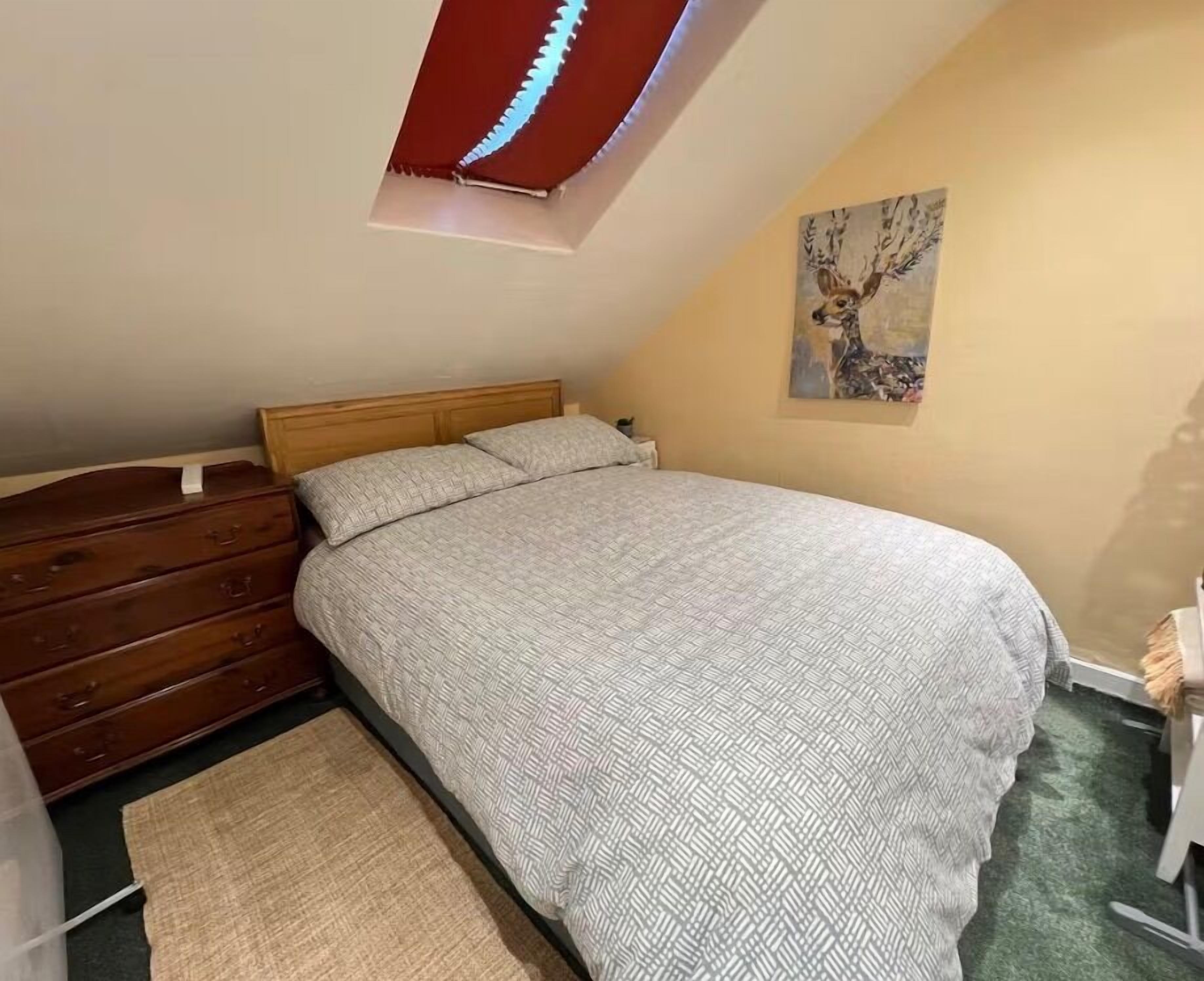 Une chambre à coucher avec un lit, une commode en bois et un tableau accroché au mur.