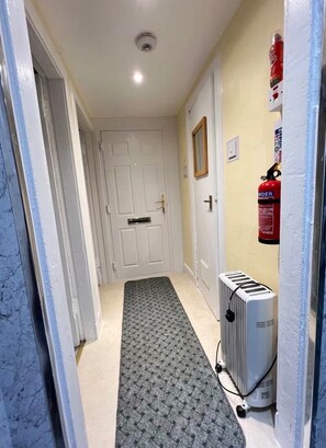 A hallway with a radiator, a fire extinguisher, and a door at the end. - Captivating 1-Bed Apartment in Largs (Largs)