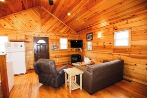 A log cabin interior with a sofa, armchair, television, and a small table. - 1 Bedroom 1 Bath Cabin with hot tub (Beaver, WV) (Beaver)
