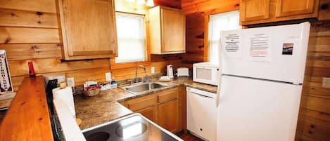 A compact kitchen with wooden walls, a stove, a sink, and a refrigerator.
