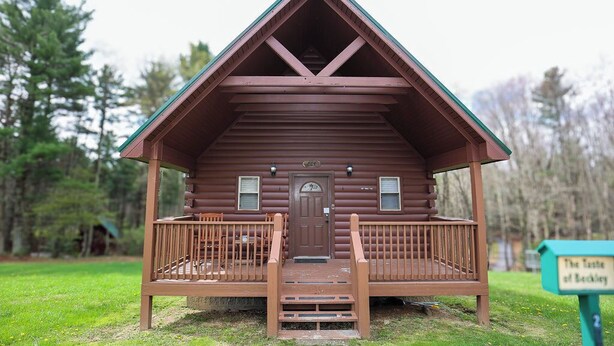 Een houten chalet met een veranda en een deur, omringd door een gazon met bomen.