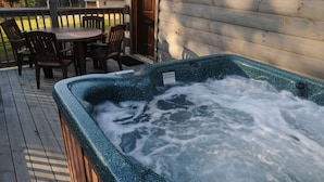 Een hottub op een houten terras, met een houten hek en stoelen op de achtergrond.