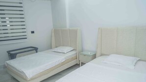 A hotel room with two beds, a bedside table, and a window with blinds.