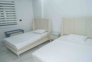 A hotel room with two beds, a bedside table, and a window with blinds.