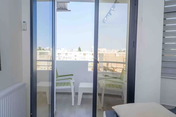 A balcony with a view of buildings, a white radiator, and two white chairs.