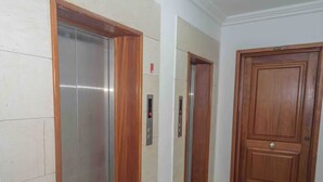 An interior corridor with two elevator doors, one metallic and one wooden, and a wooden door at the end.