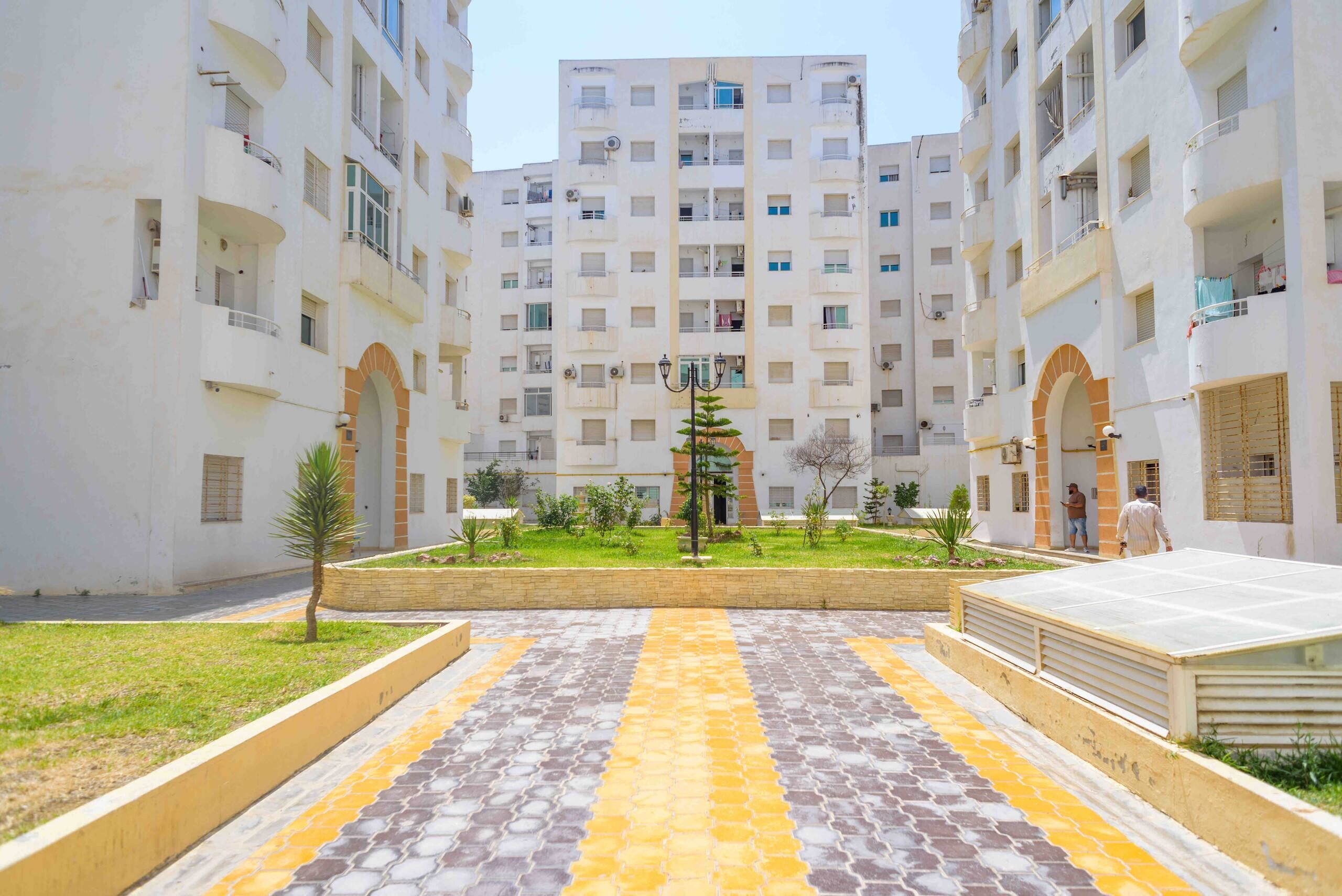 Un immeuble résidentiel à plusieurs étages, doté de balcons et d’une cour intérieure avec un sol dallé formant un motif.