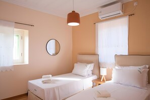 Quarto de hotel com duas camas, um espelho redondo, ar condicionado e uma janela com cortinas.
