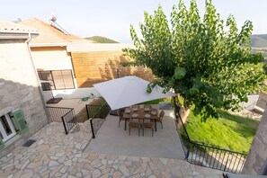 Eine Terrasse mit Tisch und Stühlen, einem weißen Sonnenschirm und einem Baum.