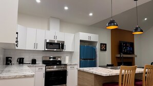 A modern kitchen with white cabinets, stainless steel appliances, a built-in oven, and a marble countertop.
