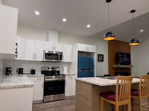 A modern kitchen with white cabinets, stainless steel appliances, a built-in oven, and a marble countertop.