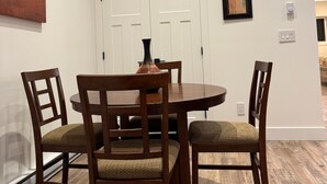 A dining area with a round table and four wooden chairs, white walls, and a door with a picture frame.