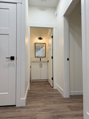 A hallway with white doors, a mirror above a sink, and wooden flooring.