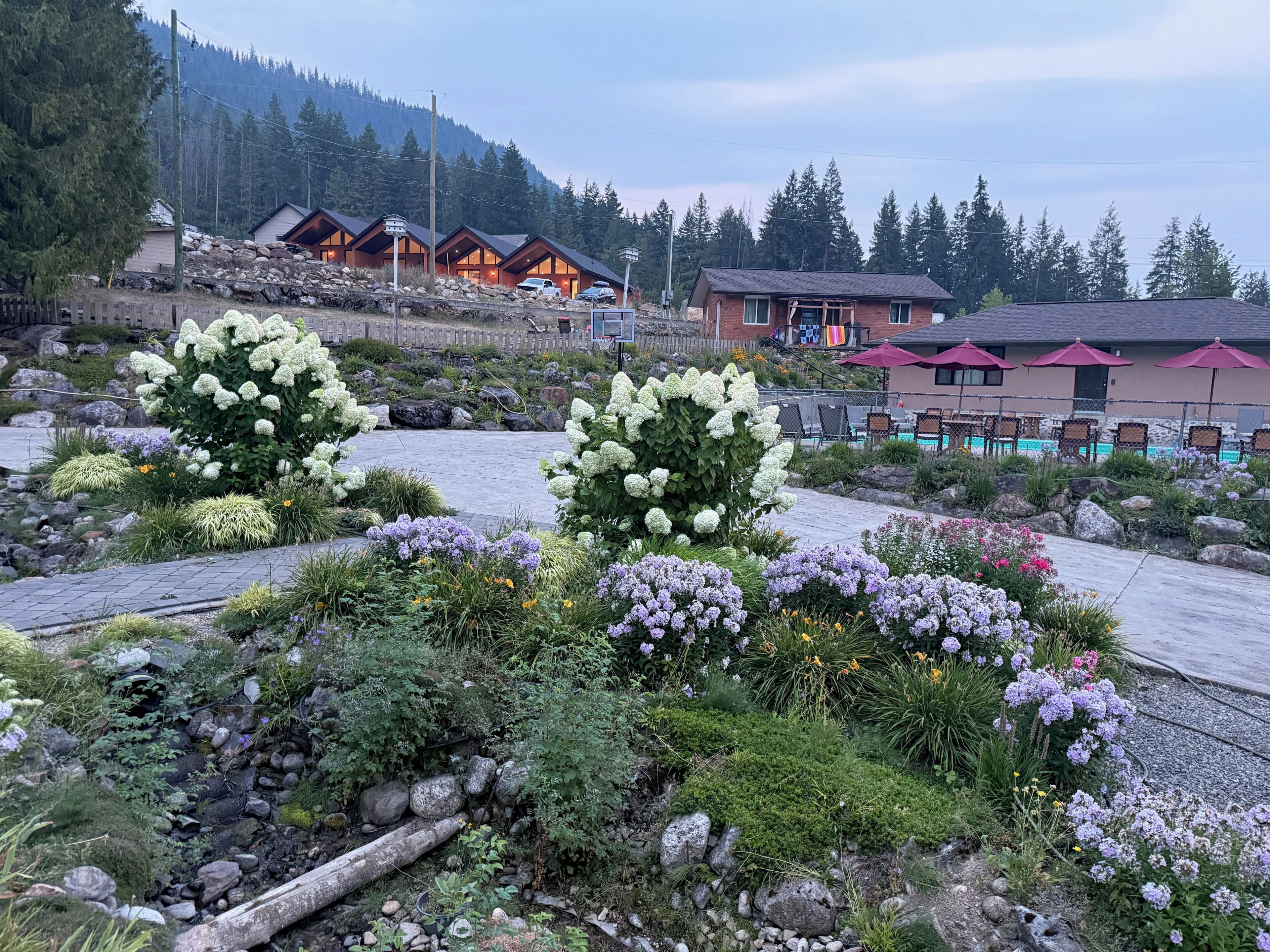 Resort com várias cabanas, piscina e jardim paisagístico com diversas plantas e flores.