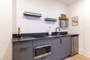 A modern kitchen with a built-in oven, a microwave, a sink, and a wine bottle on the counter. - Thena Hotel - Oversized 1 Bedroom (Philadelphia)