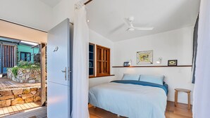 A bedroom with a bed, a ceiling fan, a window with wooden shutters, and a stone wall outside. - The Headlands Chalets - Cabin 2 (Point Lookout)