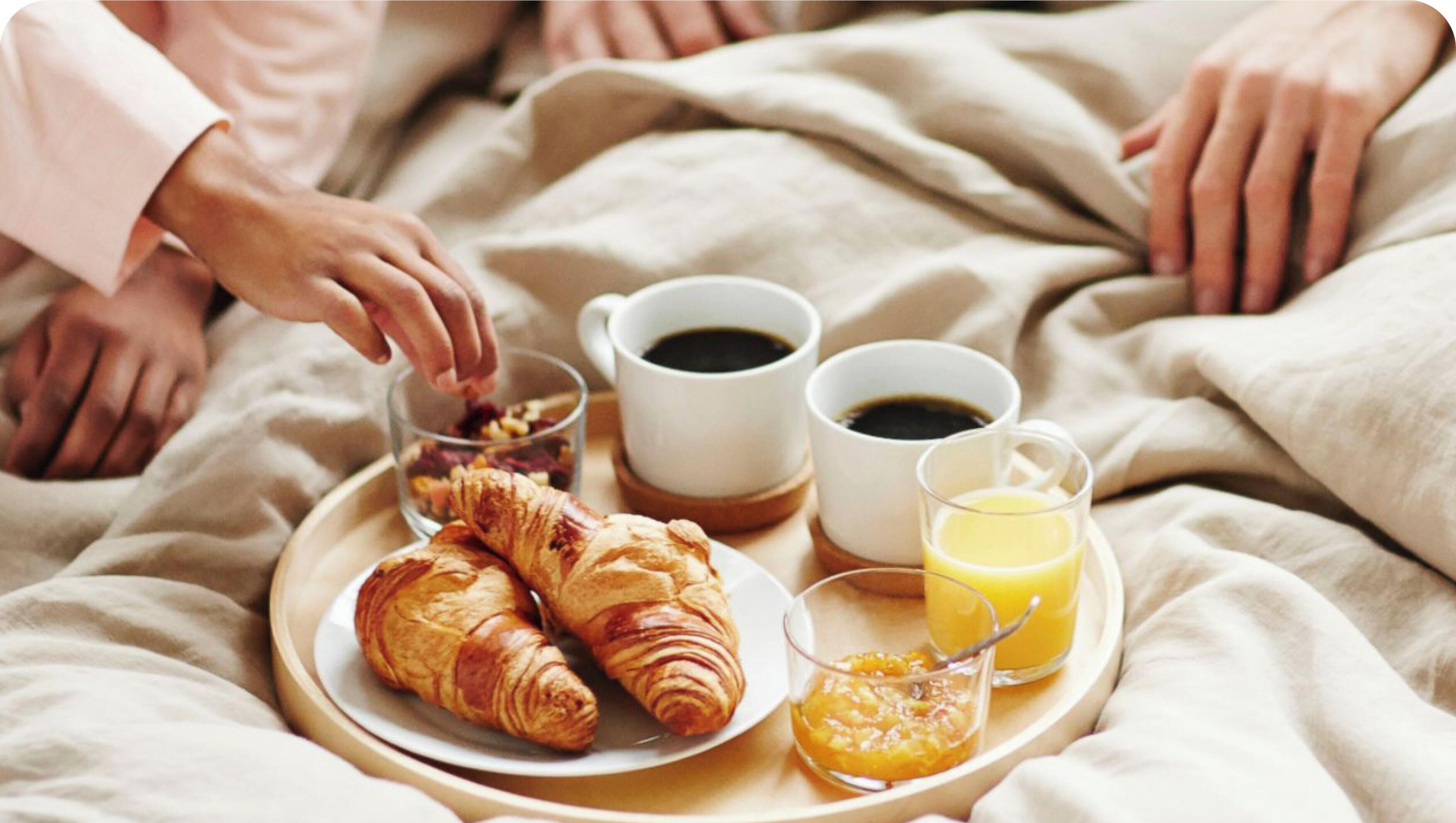 Una bandeja con croissants, tazas de café y un vaso de zumo de naranja sobre una cama.