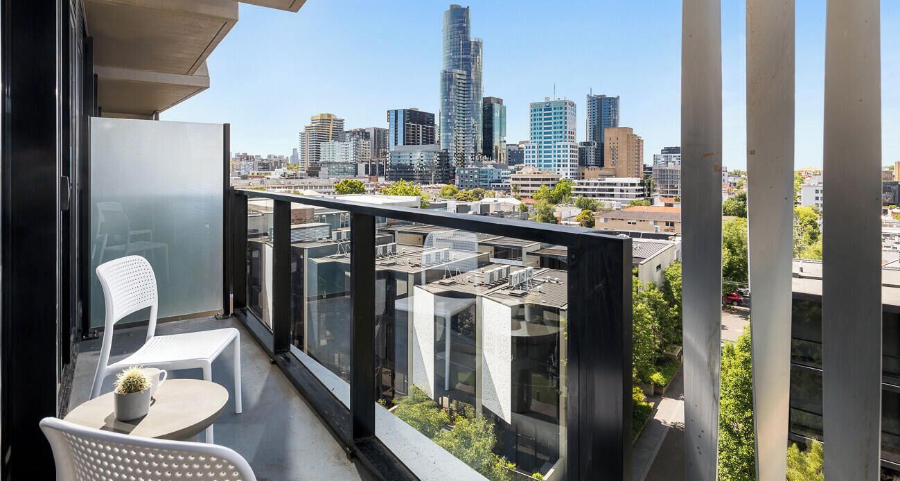 A balcony with a city view, white chairs, and a small table.