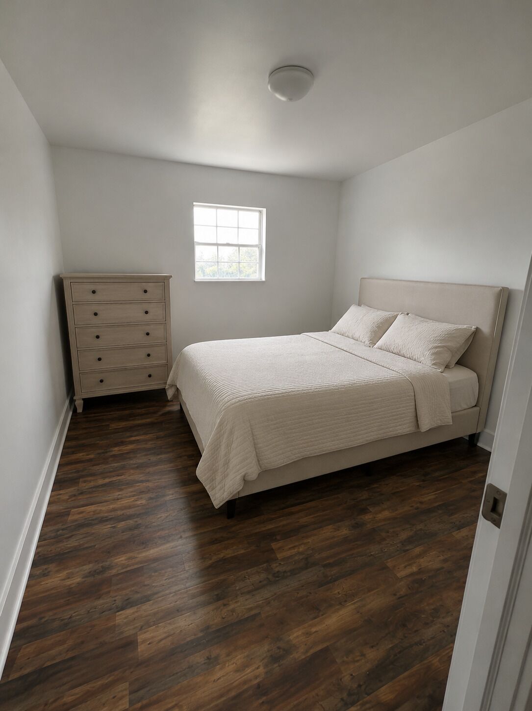A bedroom with a bed, a dresser, a window, and a ceiling light.