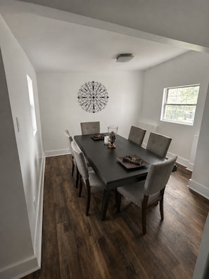 A dining room with a dark wooden table, six chairs, a decorative wall piece, and a window with natural light. - Stylish Nashville Getaway Near Downtown – Comfort, Convenience & Southern Charm! (Nashville)