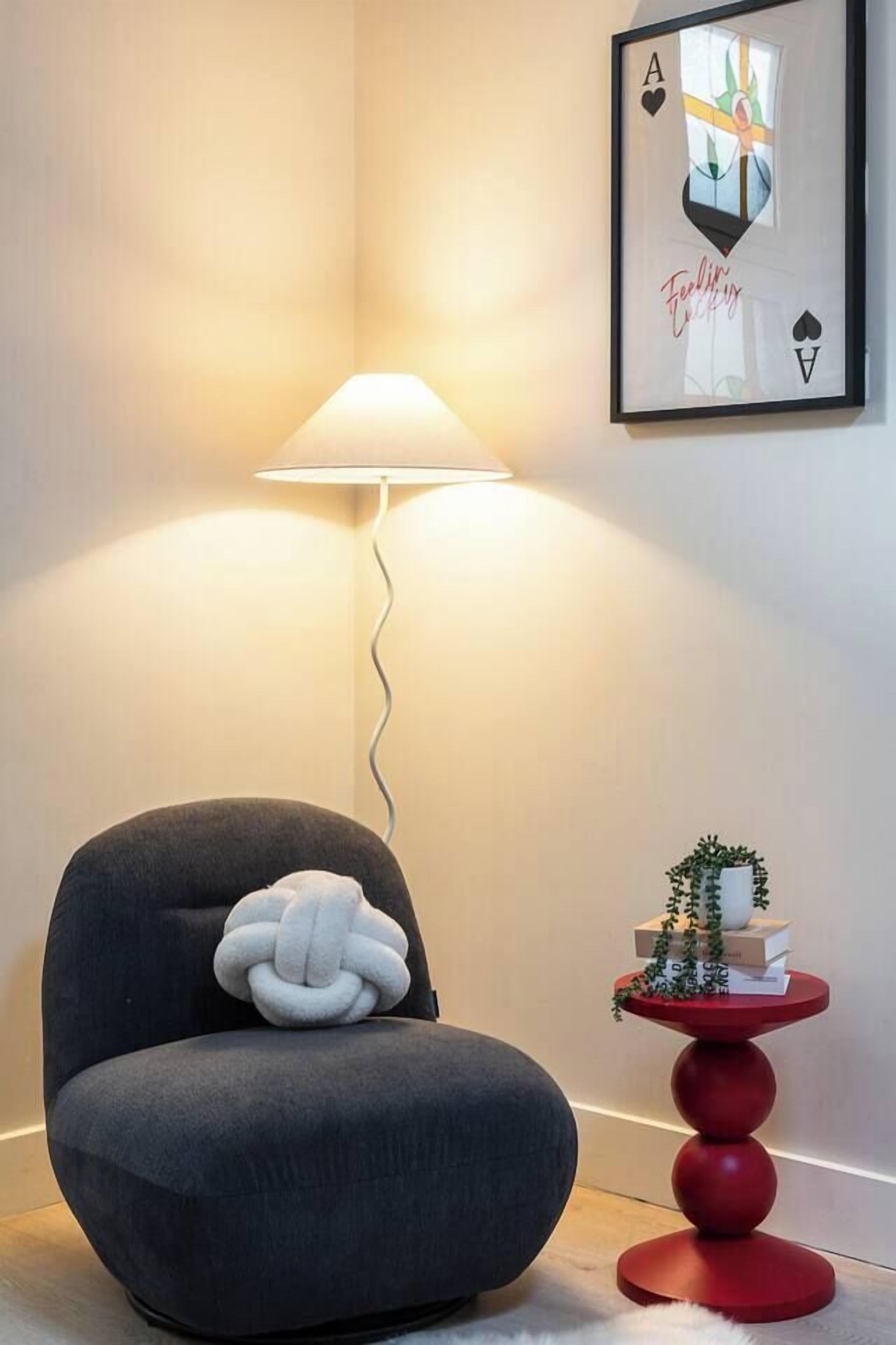 Une pièce comprenant un fauteuil de couleur gris foncé, une petite table d’appoint rouge avec une petite plante, et un tableau encadré accroché au mur.