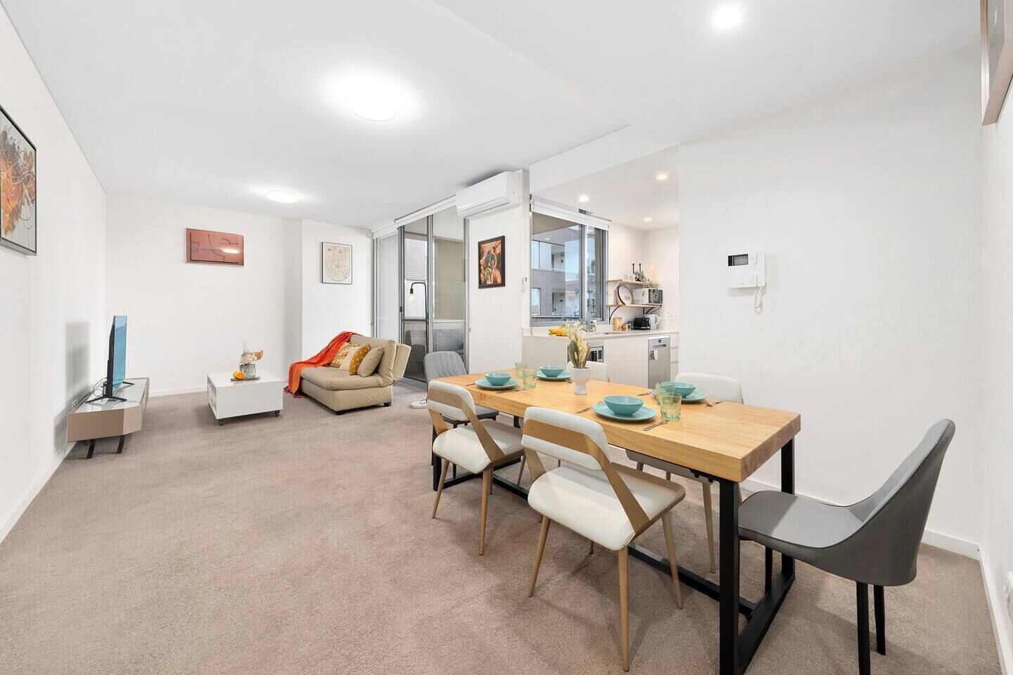A modern apartment with a dining area, a sofa, a TV, and a kitchen.