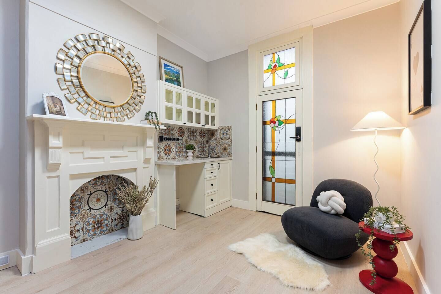 Ein Zimmer mit Kamin, Schreibtisch, Stuhl, Lampe und einer Tür mit Buntglasverzierungen.