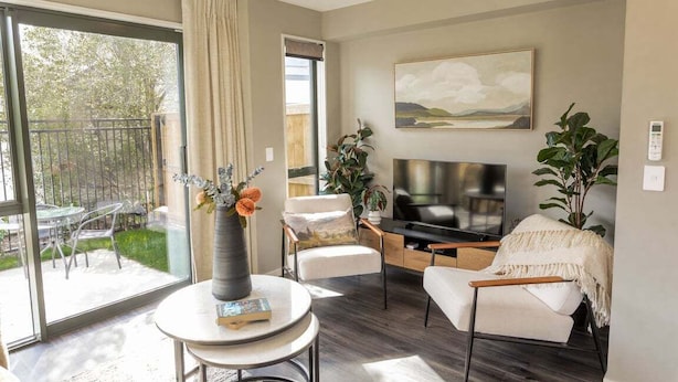 Ein modernes Wohnzimmer mit Fernseher, Sitzgelegenheiten und Blick ins Freie.