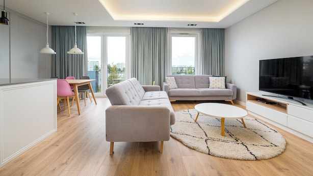 Una sala de estar moderna con sofá, una mesa de comedor con sillas, televisor y un ventanal con cortinas.