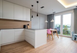 A modern kitchen with white cabinetry, a wooden countertop, and a dining area with a table and chairs. - Imielin Signature Apartment (Warszawa)