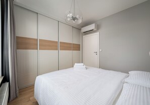 A bedroom with a large bed, a wardrobe, and an air conditioning unit. - Imielin Signature Apartment (Warszawa)