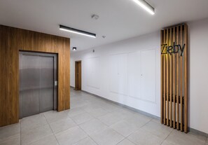 A hallway with a wooden door, a wall-mounted sign, and a tiled floor. - Imielin Signature Apartment (Warszawa)