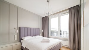 Un dormitorio moderno con una cama grande, una lámpara de noche y vistas de la ciudad a través de una ventana.
