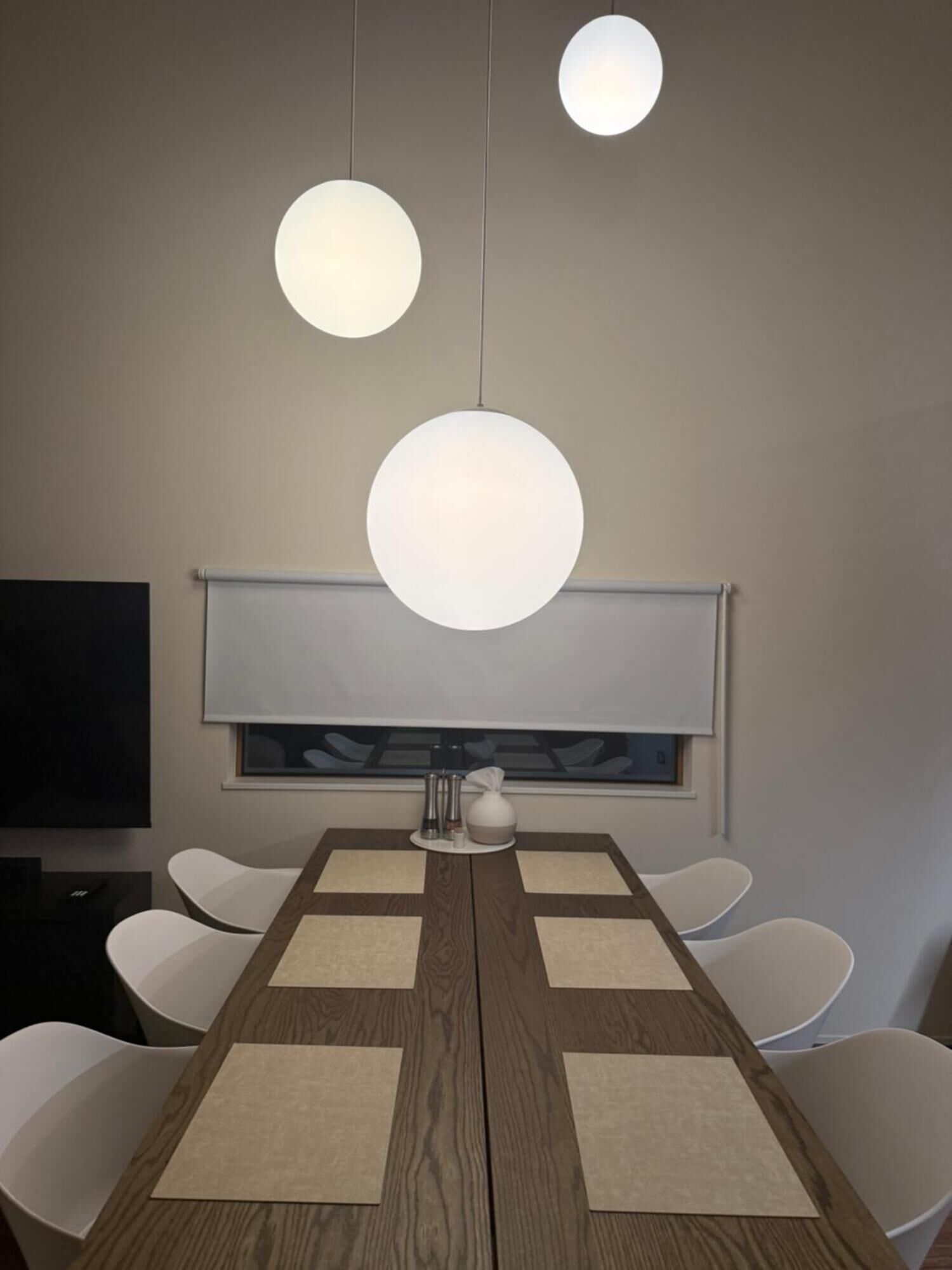 A dining area with a wooden table, white chairs, and pendant lights.