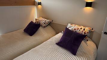 Deux lits simples avec des têtes de lit, une fenêtre donnant sur un espace verdoyant et des lampes fixées au mur.