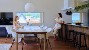 Cozinha moderna com área de refeições, TV e vista para um bairro residencial.