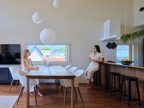 A modern kitchen with a dining area, a TV, and a view of a residential area. - HIRUGANO LAPLAND Santa's home in Japan (Gujo)