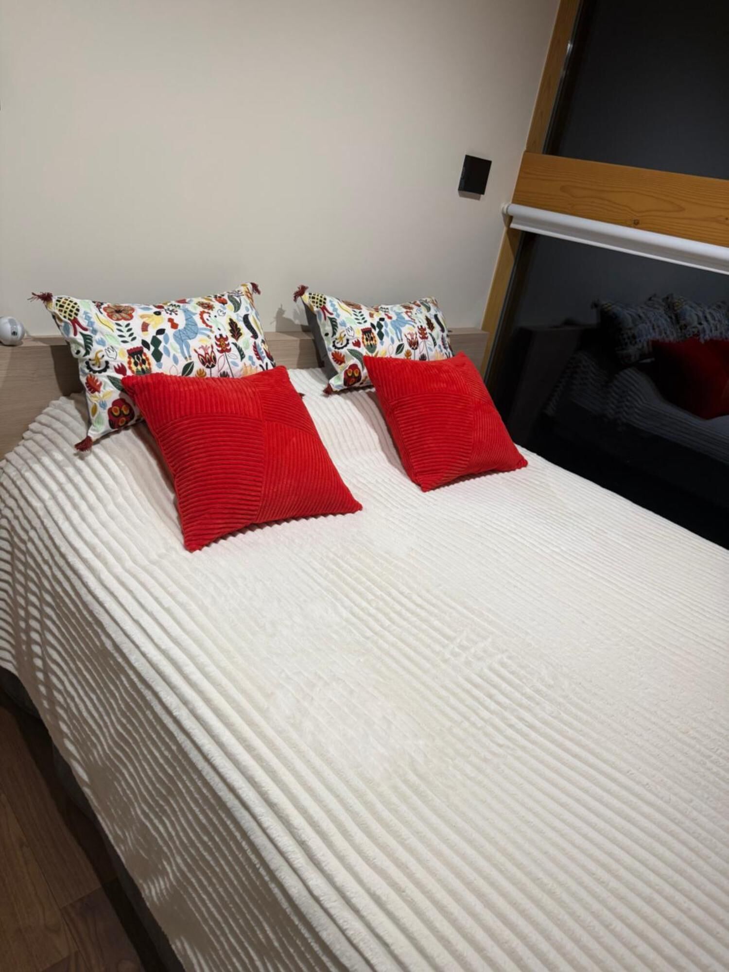 A bed with a white textured bedspread and two red pillows.