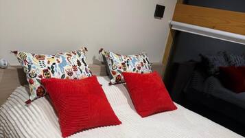 A bed with a white textured bedspread and two red pillows.