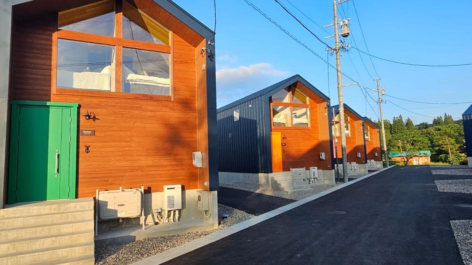 A row of cabins with wooden exteriors, a green door, and outdoor electrical boxes.