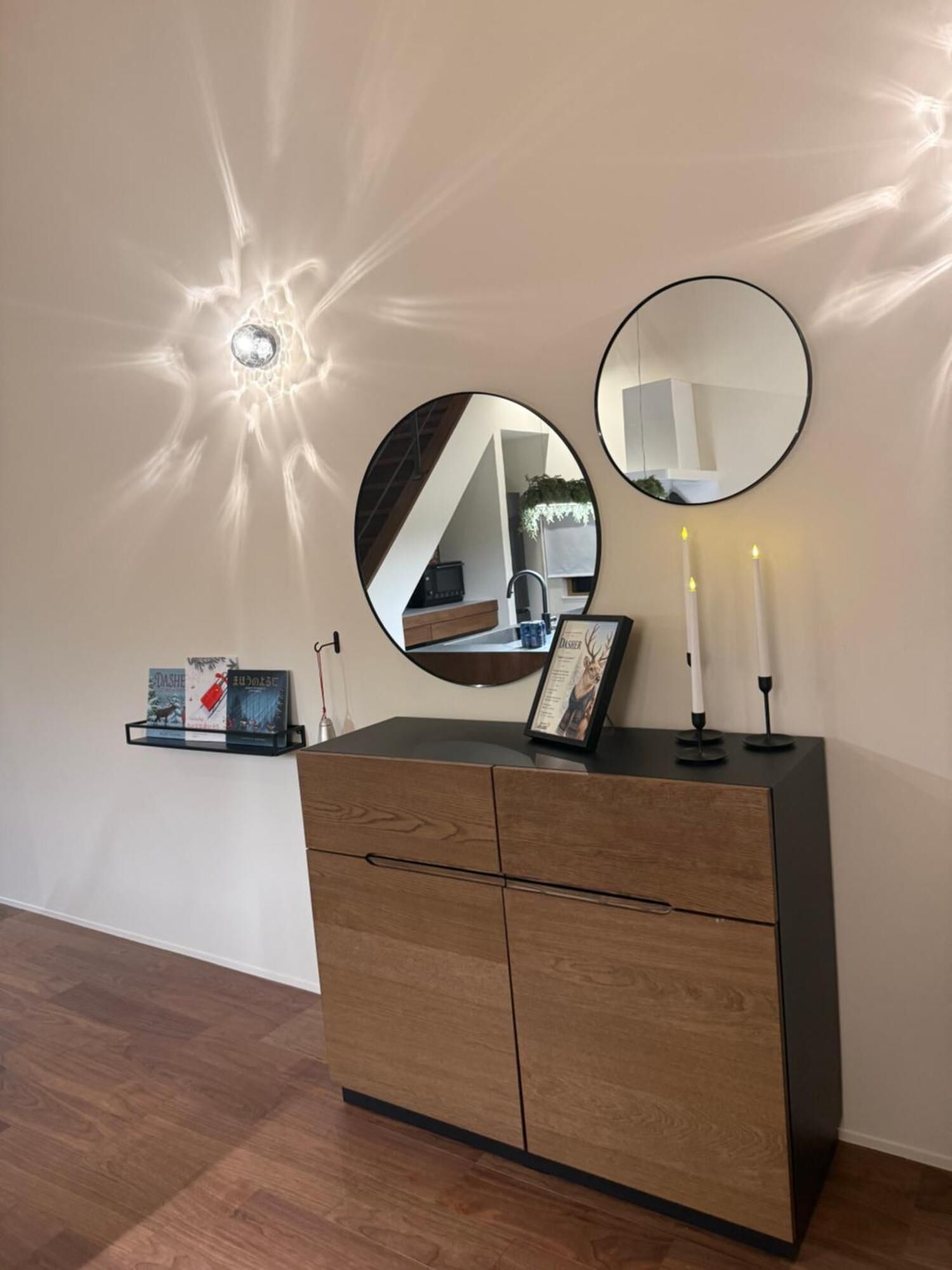A wooden dresser with two round mirrors, a framed picture, and two lit candles on a wall.