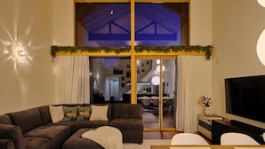 Uma sala de estar moderna com sofá seccional, TV de tela plana e uma grande janela com vista para o interior.