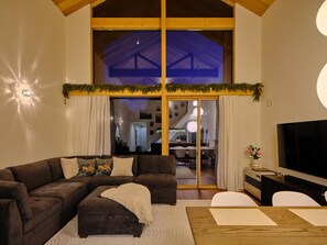 A modern living room with a sectional sofa, a flat-screen TV, and a large window with a view of the interior. - HIRUGANO LAPLAND Santa's home in Japan (Gujo)