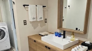 Casa de banho moderna com toucador de madeira, espelho grande e máquina de lavar roupa embutida.