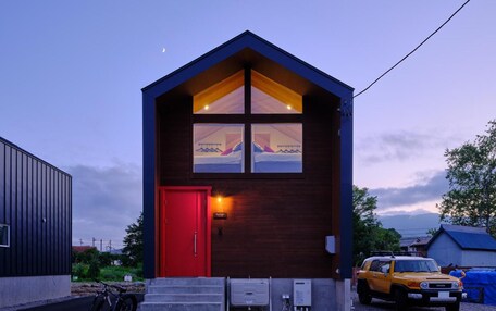 A small, modern building with a red door, a staircase leading to the entrance, and a vehicle parked outside.