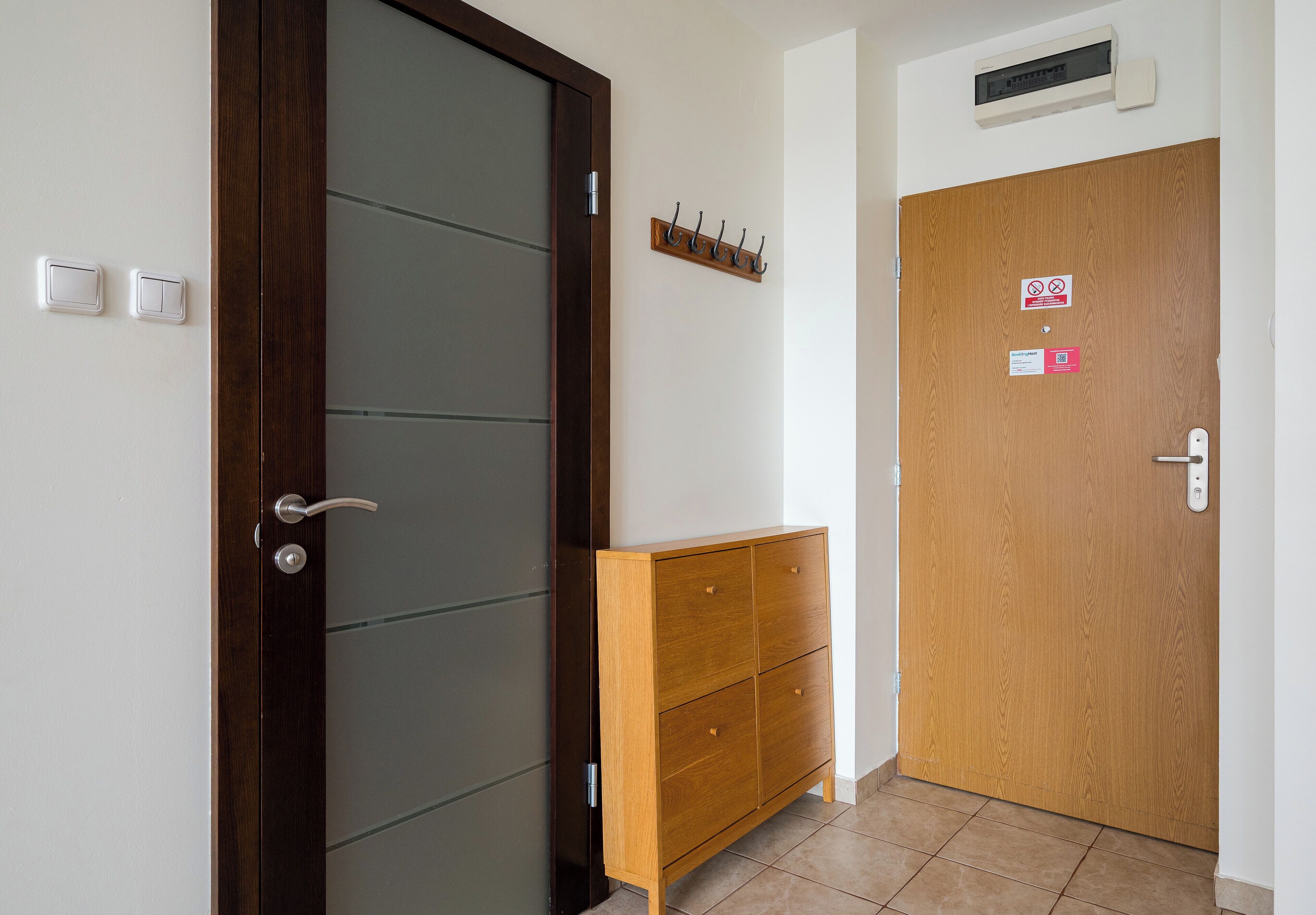 Een hotelkamer met een houten kast, een donkere deur, een lichtschakelaar en een bordje met een rookverbod.